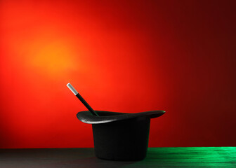 Magician's hat and wand on black wooden table against color background, space for text