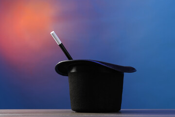 Magician's hat and wand on wooden table against color background