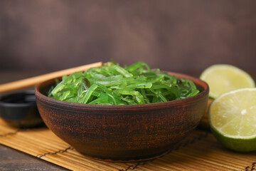 Tasty seaweed salad in bowl served on table against brown background, closeup