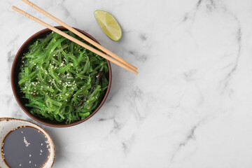 Tasty seaweed salad in bowl served on white marble table, flat lay. Space for text