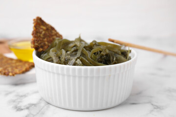 Tasty seaweed salad in bowl served on white marble table, closeup