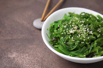 Tasty seaweed salad in bowl served on brown table, closeup. Space for text