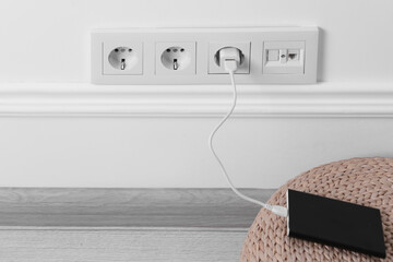Power bank plugged into electric socket on white wall