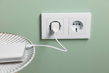 Power bank plugged into electric socket on light green wall