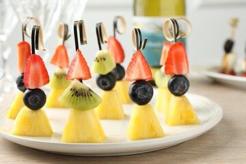 Tasty canapes with pineapple, kiwi and berries on light wooden table, closeup