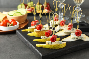 Tasty canapes with pears, blue cheese and prosciutto on grey table, closeup