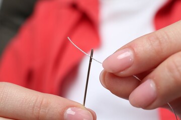 Woman inserting thread through eye of needle, closeup