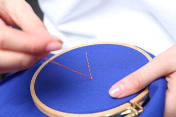 Woman with sewing needle and thread embroidering on cloth, closeup