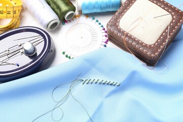 Light blue cloth with needle, thread and stitches near sewing tools on table, above view