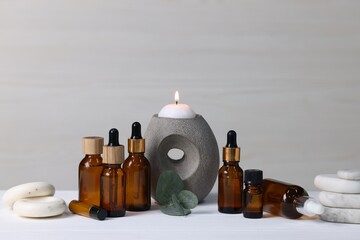 Different aromatherapy products, burning candle and eucalyptus leaves on white wooden table against...