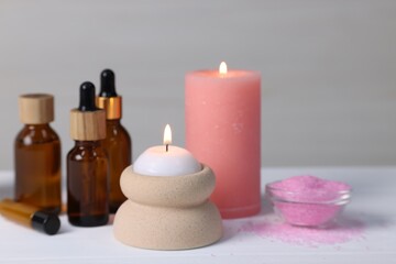 Different aromatherapy products and burning candles on white wooden table, closeup