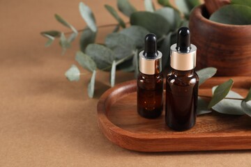 Aromatherapy. Bottles of essential oil and eucalyptus leaves on brown table, closeup. Space for text