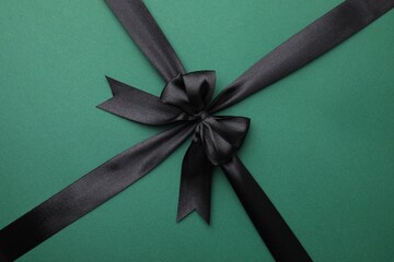 Black satin ribbon with bow on green background, top view