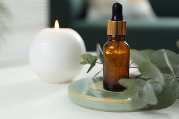 Aromatherapy. Bottle of essential oil, burning candle and eucalyptus leaves on white table