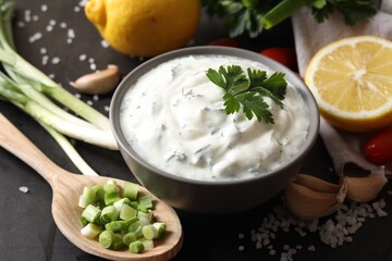 Delicious yogurt in bowl and ingredients on black table, closeup