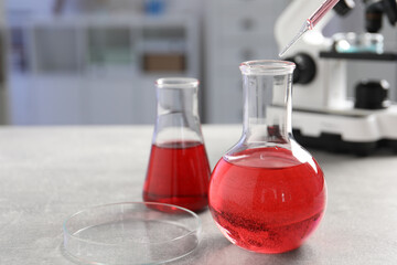 Laboratory analysis. Flasks with red liquid, petri dish and microscope on light grey table