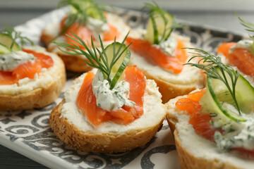 Tasty canapes with salmon, cucumber, cream cheese and dill on table, closeup
