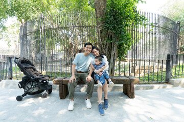 Asian parent with son sitting on wood bench at zoo