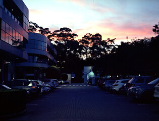 A modern glassed building and parking full of the cars in the sunset. Medium format film (Kodak...