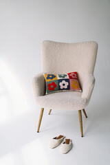 A cozy armchair sits next to a sleek white canvas in a brightly lit studio setting. A pair of...