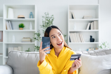 Young asian woman lying on sofa in living room, makes online banking payments through the internet...