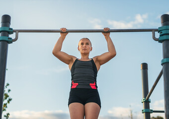 woman athlete doing pull ups on a bar outdoors. calisthenics