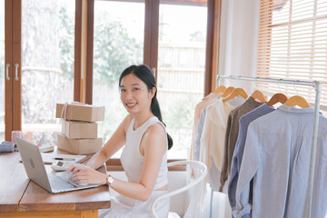 Beautiful Asian female fashion designers or dressmakers show the sample clothes to the client in the online meeting. Fashion designer working in the studio. Small business concept