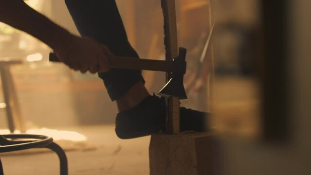 Carpenter cutting wood with axe on log in workshop