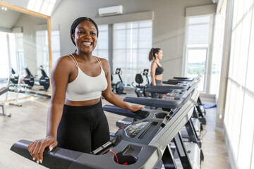Healthy strong female African American plus-size sportswear exercise running treadmill fitness in...