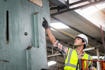 Male industrial engineer wearing helmet and safety vest, pointing away at manufacturing plant...