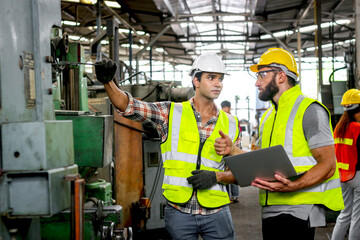 Industrial foreman and worker with helmet and safety vest using laptop computer during discussing...