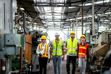 Group of industrial foreman engineer and workers with helmet and safety vest walking past to inspect machinery engine and production process at manufacturing industry factory. Teamwork at workplace