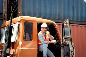 Happy smiling handsome foreman with helmet and safety vest holding walkie talkie and giving thumb...