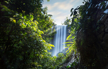 large waterfall though a lush forest, with lightbeams