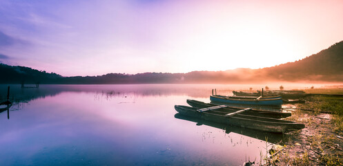 reflective calm lake at sunrise with fog and small rowing boats