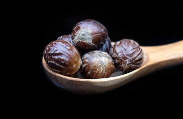Closeup of Nutmeg or Javitri in a Wooden Spoon Isolated on Black Background with Copy Space, Also Known as Myristica Fragrans