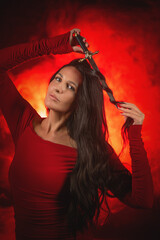 Young beautiful girl with dark hair and in the red dress posing in the dark background with the...