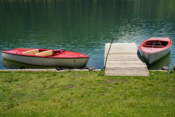 A wooden jetty and two red boats on the lake shore of Walchsee, Tyrol, Austria.