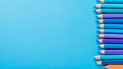 Fototapeta premium A collection of colored pencils aligned on a blue surface, enabling text inscription area