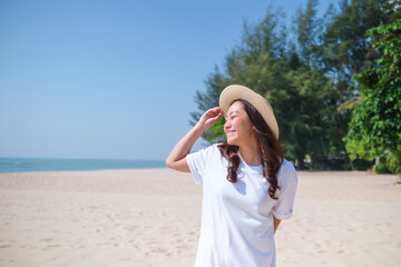 Portrait image of a young woman with white t-shirt and hat strolling on the beach with the sea and...