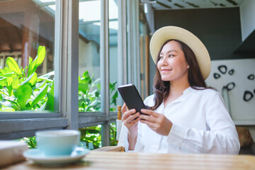 Portrait image of a beautiful young woman with hat holding and using mobile phone