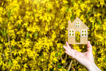 Naklejka premium The girl holds the house symbol against the background of blossoming forsythia 