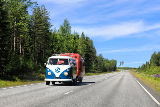 Volkswagen Type 2 (T1) Transporter van with split windshield pulls old caravan on highway on a beautiful day of summer. 