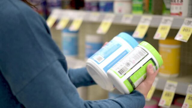 Woman choose sport nutrition in specialty store. Hold in hands and reeds information about the goods on it.   Vitamins, protein, dietary supplements and other substances for health of athletes and ord