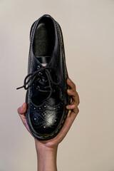 A man's hand holds full black brogue wingtip shoes with a rubber outsole made of genuine cow...