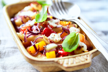 Penne pasta baked with peppers, red onion and mozzarella. Bright wooden background.