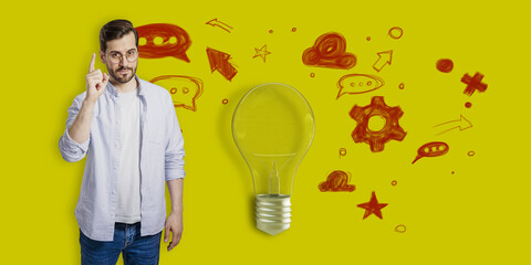 Attractive thoughtful young businessman pointing up at creative light bulb sketch with icons on...