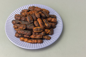 Sweet, spicy tamarind tree fruit in a round plate on a gray background
