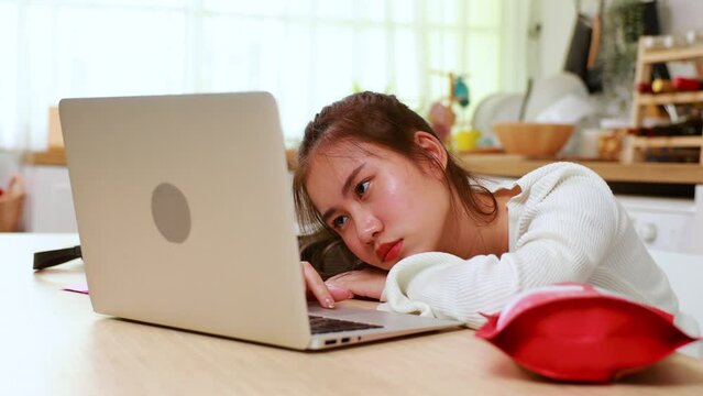 bored Tired exhausted, fatigue and fell asleep. Yaoung asian thai female working on laptop in kitchen room at home. Overwork. Exhausted woman  sleeply eye at workplace