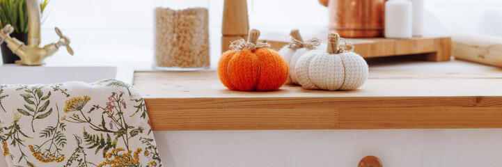 A kitchen counter with a white cabinet and a towel with a floral design. There are two pumpkins on...